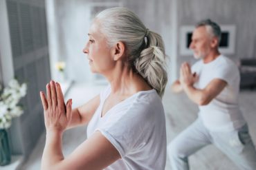 Photographie d'un couple de seniors habillés en vétements de sport et réalisant une séance de yoga à domicile
